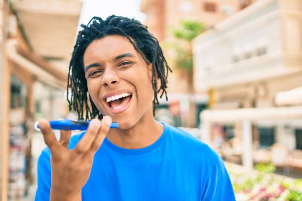 giovane afroamericano che invia un messaggio audio usando lo smartphone in strada della città. - spanish culture audio foto e immagini stock