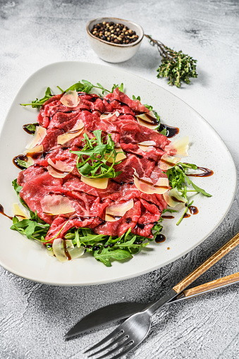 Beef carpaccio on white plate with parmesan cheese and arugula. Gray background. Top view