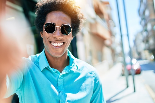 Young handsome african american man wearing casual clothes and sunglasses smiling happy. Making selfie by the camera at town street.