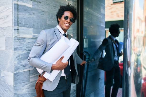 istock Young handsome african american architect man smiling happy. Standing with smile on face holding blueprints at the office door. 1288609818