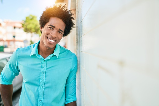 Young handsome african american man wearing casual clothes smiling happy. Looking at the camera leaning on the wall at town street.