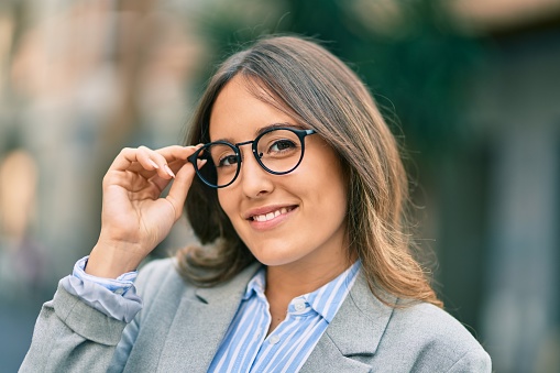 Young hispanic businesswoman smiling happy touching her glasses at the city.