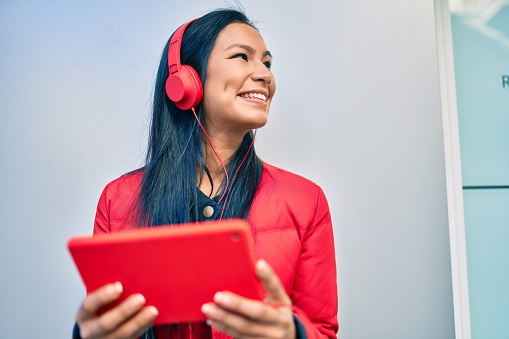 Young latin woman smiling happy using headphones and tablet walking at the city.
