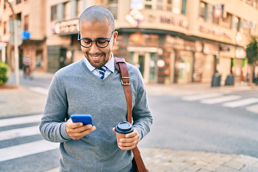 Young african american businessman using smartphone and drinking take away coffee at the city.