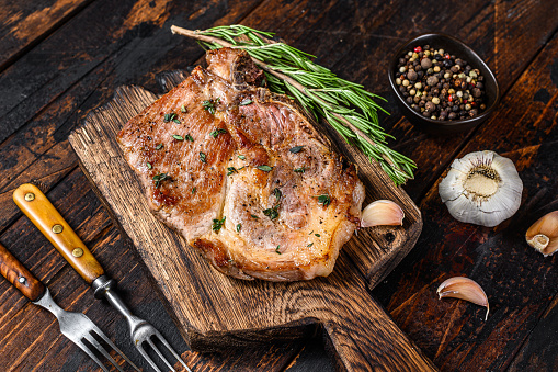 Roasted pork chop steak on a cutting board. Dark wooden background. Top view.