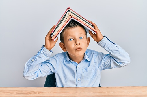caucasian kid holding book on head looking at the camera