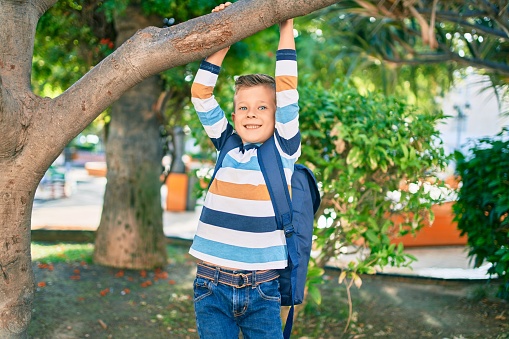 Adorable caucasian student boy smiling happy hanging on tree branch at the park.