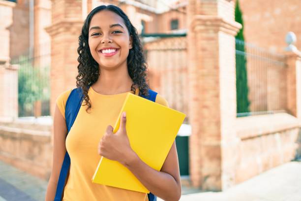 젊은 아프리카 계 미국인 학생 소녀는 대학 캠퍼스에서 책을 들고 행복한 미소. - student printed media walking clothing 뉴스 사진 이미지