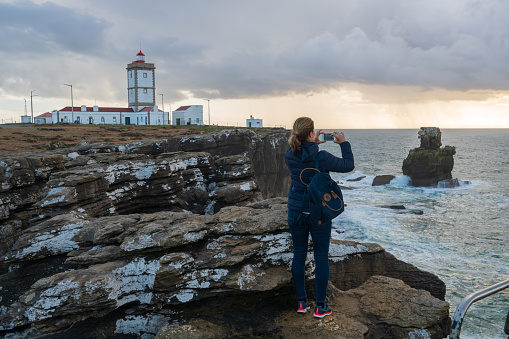 Peniche, Portugal - November 20, 2018 : Caucasian woman photographing landscape of Cabo Carvoeiro Lighthouse cape in Peniche, Portugal