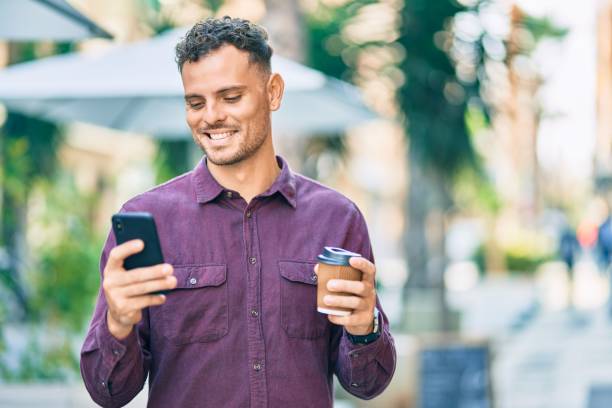 istock Young hispanic man using smartphone and drinking coffee at the city. 1288616637