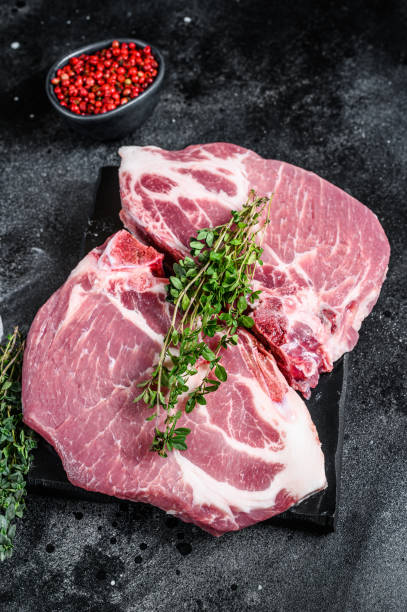 istock Raw pork meat steaks on a marble board. Black background. Top view 1288616787