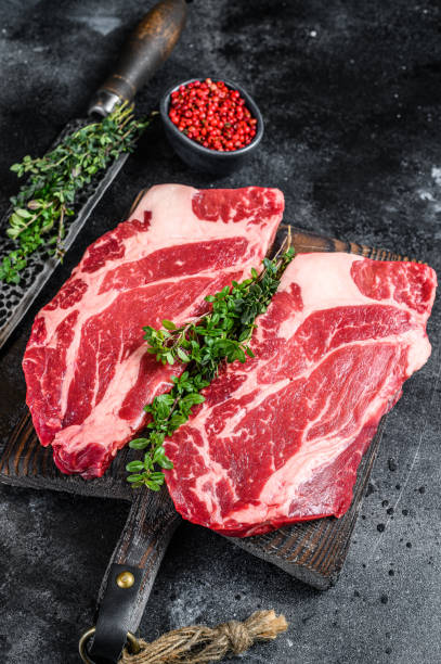 istock Raw chuck eye roll steaks premium beef meat on a cutting board. Black background. Top view 1288617052