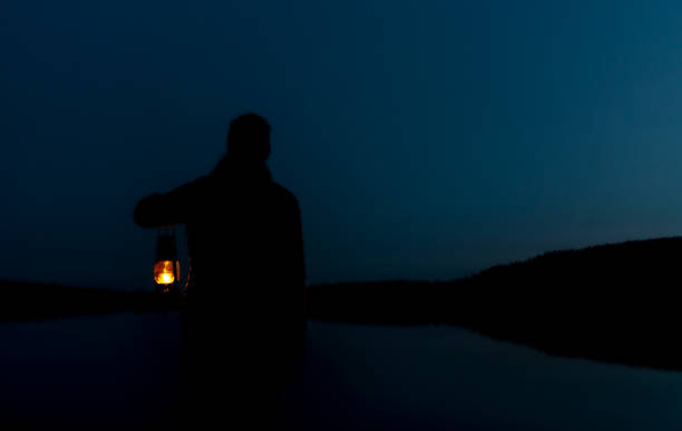 一日の最後の光を野生の湖で見てい��る女性のシルエットで、火のついたヴィンテージ灯油ランプを持っています。 - oil lantern ストックフォトと画像