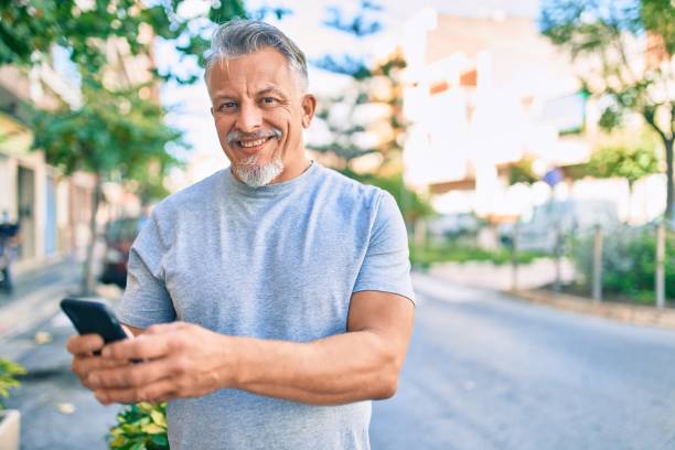 istock Middle age hispanic grey-haired man smiling happy using smartphone at the city. 1288618066