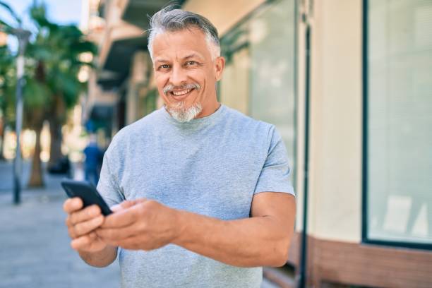 istock Middle age hispanic grey-haired man smiling happy using smartphone at the city. 1288618125