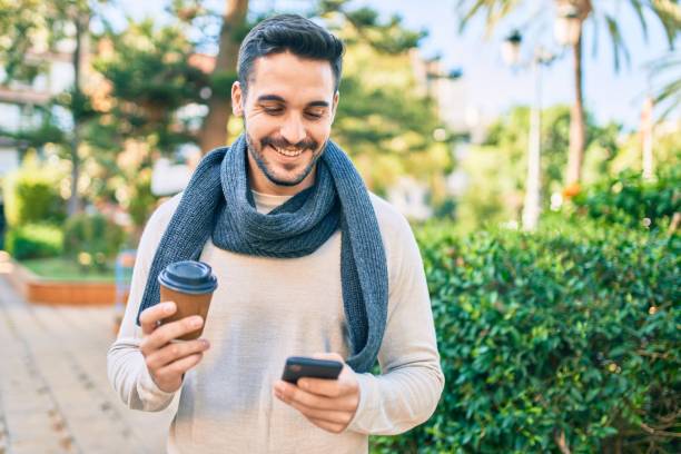 istock Young hispanic man smiling happy using smartphone and drinking take away coffee at the park. 1288618317
