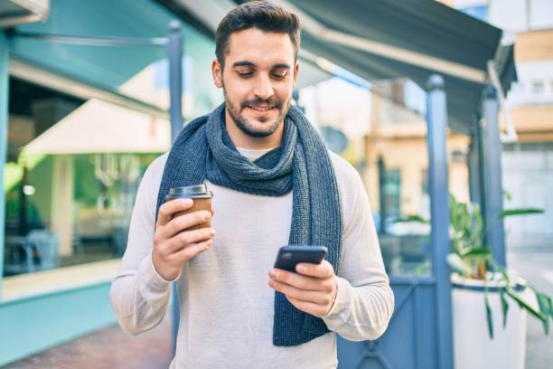 istock Young hispanic man smiling happy using smartphone and drinking take away coffee at the city. 1288618362
