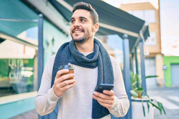 istock Young hispanic man smiling happy using smartphone and drinking take away coffee at the city. 1288618369