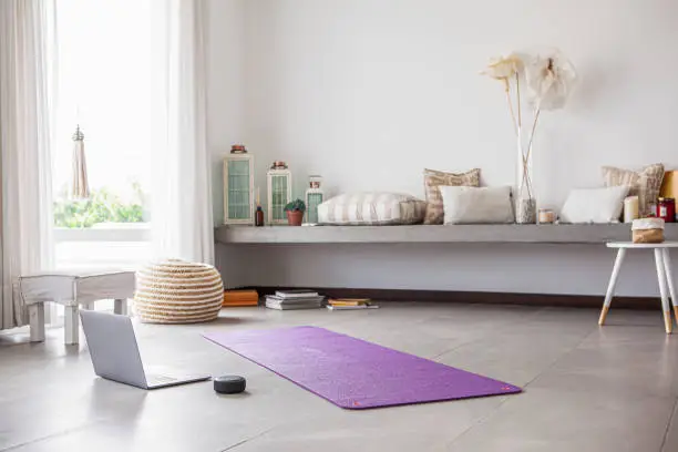 Interior view of modern living room with laptop exercise mat and smart speaker on floor