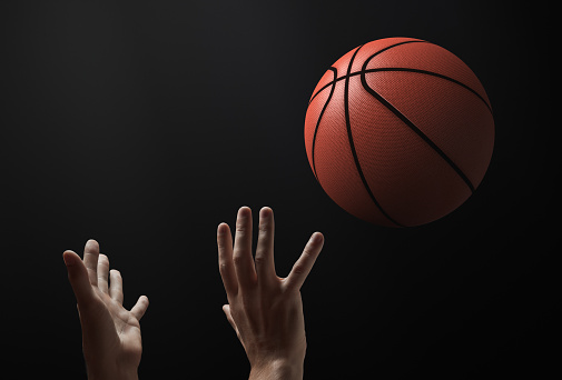 Basketball theme. The moment the ball is thrown. There are only hands and a ball in the frame. Dark background