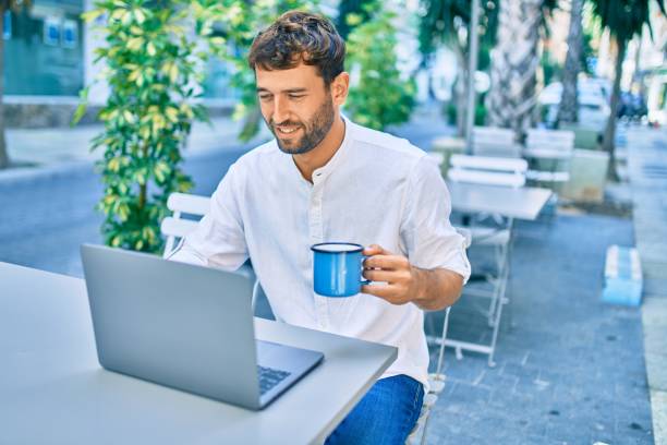 istock Handsome man with beard wearing casual white shirt on a sunny day working using laptop at cafeteria 1288623020