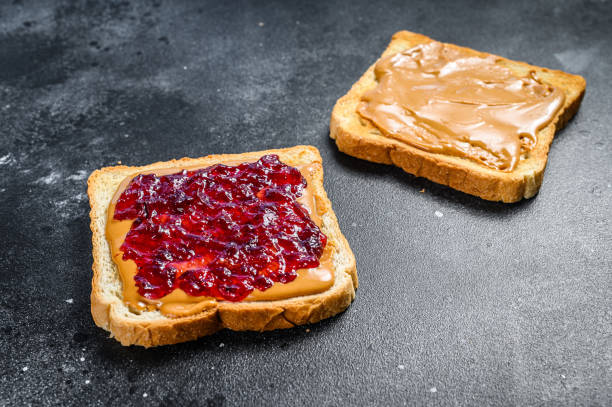 istock Peanut butter and jelly on white bread toasts.  Black background. Top view 1288625540