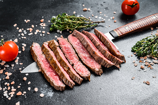 Grilled and sliced flat iron rare steak. Marble beef meat. Black background. Top view.