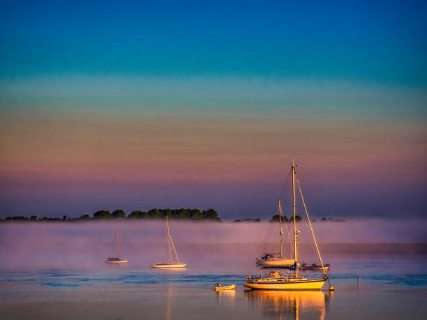 small boats at anchor in morning mist with early morning sunlight on river alde with pale pastel coloured sky, aldeburgh, suffolk, england, britain - east anglia imagens e fotografias de stock