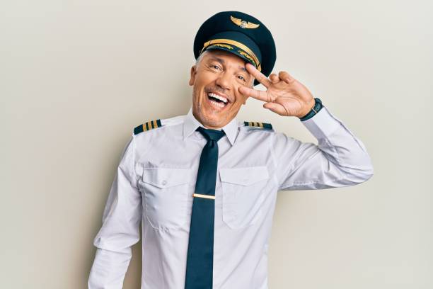 Handsome middle age mature man wearing airplane pilot uniform doing peace symbol with fingers over face, smiling cheerful showing victory