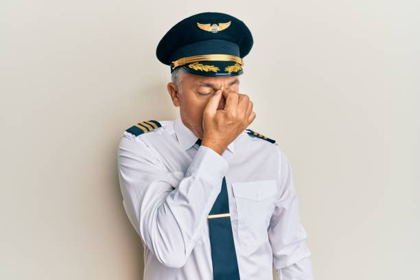 飛行機のパイロットの制服を着たハンサムな中年の成熟した男は、疲労と頭痛を感じる鼻と目をこすり疲れました。ストレスとフラストレーションの概念。 - male senior adult men portrait ストックフォトと画像