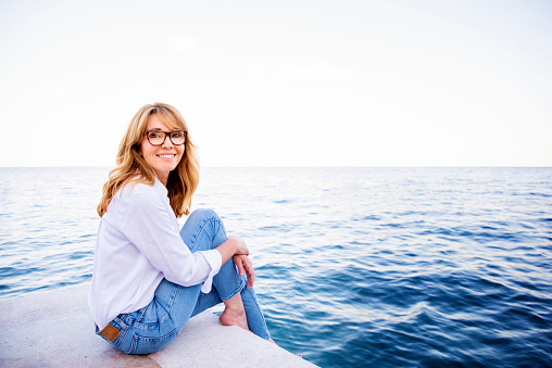 Hermosa mujer madura sentada en el acantilado y relajándose junto al mar photo