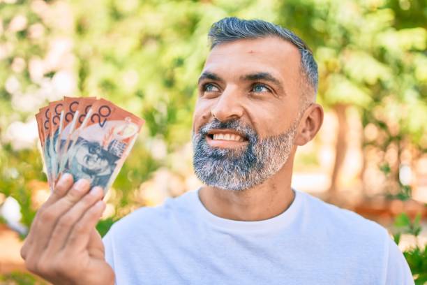 istock Middle age grey-haired man smiling happy holding australian dollars banknotes standing at the park 1288631492