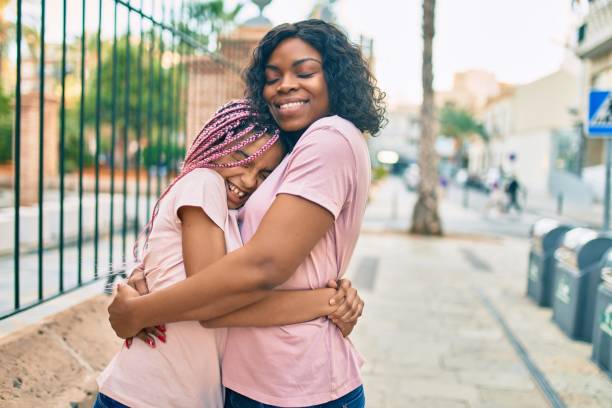 Beautiful african american mother and daughter smiling happy and hugging. Standing with smile on face standing at the city. Beautiful african american mother and daughter smiling happy and hugging. Standing with smile on face standing at the city. parenting stock pictures, royalty-free photos & images