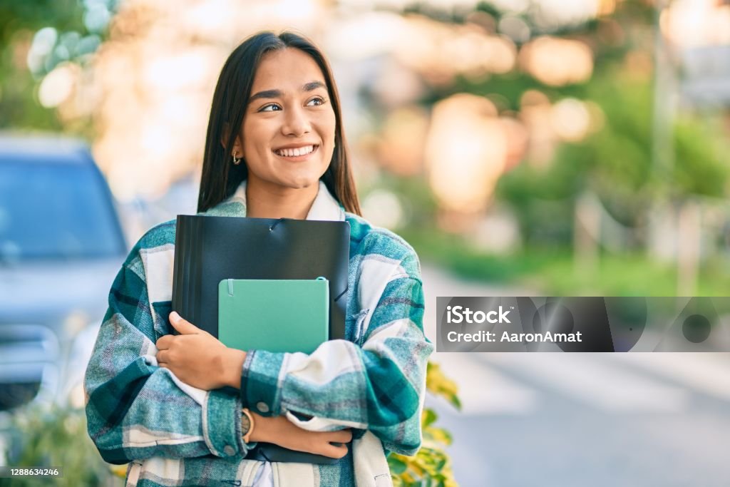 Young latin student girl smiling happy holding folder at the city. University Student Stock Photo