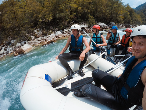 Big family with kids having a great fun while rafting and rowing on the fast river.