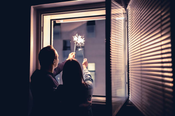 paar hält funkeln aus dem fenster in der nacht. silvesterfeier, jubiläum, party oder date zu hause. spontaner spaß mit leichtem feuerwerksstab. - sparkler sparks new years eve human hand stock-fotos und bilder