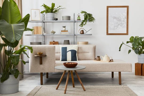 istock Cozy interior with stylish sofa, design coffee table, bookcase, plants, carpet, decoration, mock up poster map and elegant personal accessories. Neutral living room in classic house. Template. 1288636066