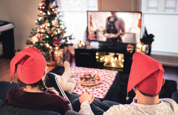 クリスマスにテレビを見ているカップル。自宅で幸せな家族の休日。木、装飾、ライト、ろうそく、テレビでリラックスソファの上の男女。現代の都市のお祝い。 - home movie ストックフォトと画像