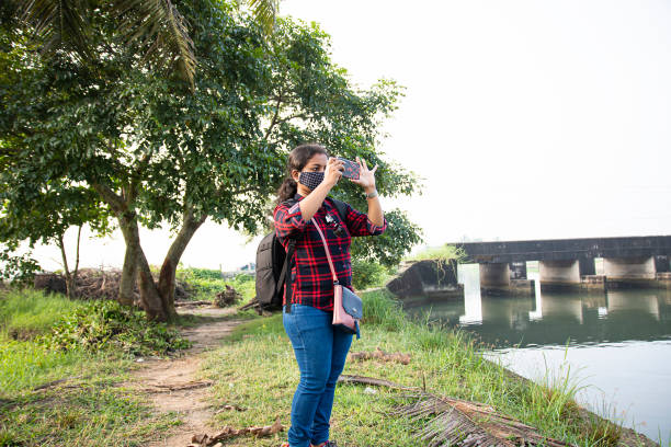 istock a Kerala backpack explorer women wearing face mask taking photos using her phone on white blur green background from kadamakudy Kerala India. the natural beauty of this place is amazing women's day ,women entrepreneur 1288636492