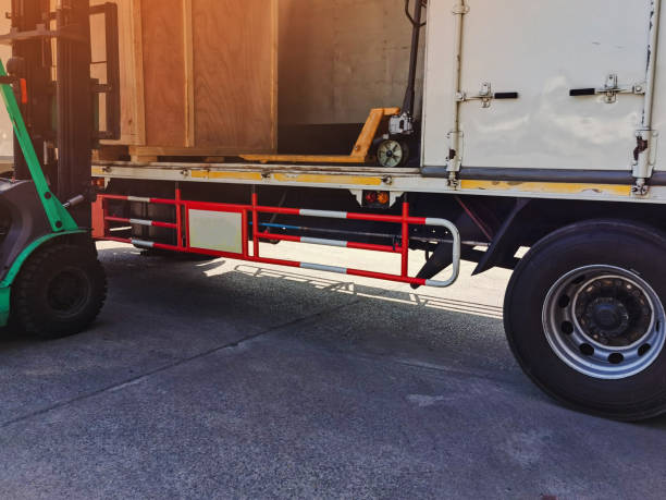istock Worker driving forklift loading shipment carton boxes goods on wooden pallet at loading dock from container truck to warehouse cargo storage in freight logistics, transportation industrial, delivery 1288643360