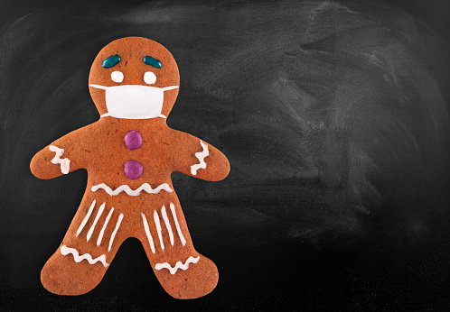 Classic gingerbread cookie man with medical mask on blackboard