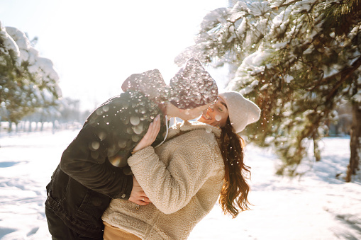 Loving couple hugging and kissing in snow forest. Enjoying time together. The concept of youth, love and lifestyle. Winter holidays.