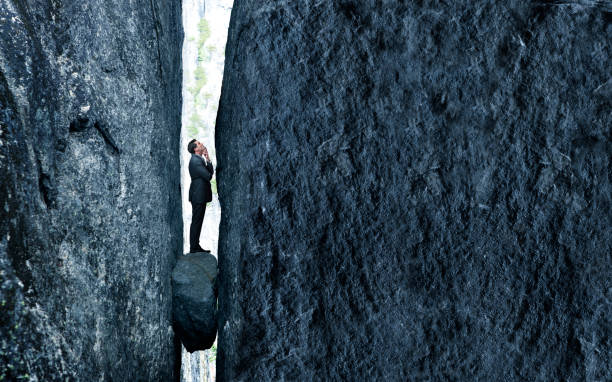Stuck Between A Rock And A Hard Place A businessman stands with a look of concern as he is trapped between a rock and a hard place. stuck stock pictures, royalty-free photos & images