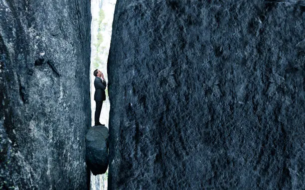 A businessman stands with a look of concern as he is trapped between a rock and a hard place.