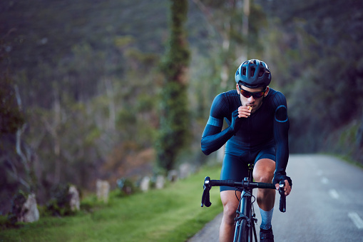 Young cyclist riding bicycle and eating snack bar outdoors on a mountain asphalt road