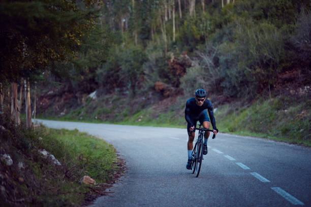 ciclista profesional andando en bicicleta por una carretera de asfalto forestal - triathlete fotografías e imágenes de stock