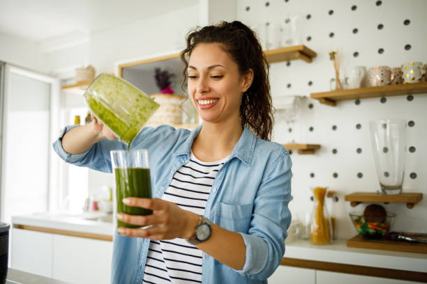 giovane donna che prepara un frullato verde a casa - women juice drinking breakfast foto e immagini stock