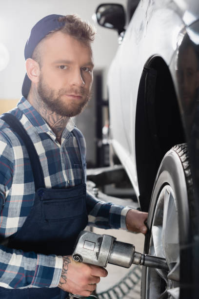 istock young mechanic looking at camera while fixing car wheel with pneumatic wrench 1288655517