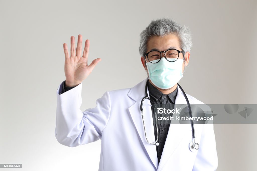 Physician The senior Asian physician with mask on the white background. Waving - Gesture Stock Photo