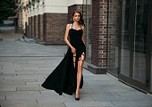 Young beautiful woman in a long black dress is walks down the street.